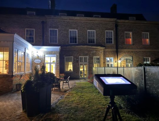 A DarkFlight unit deployed on a tripod at night during a real bat survey, lit building behind